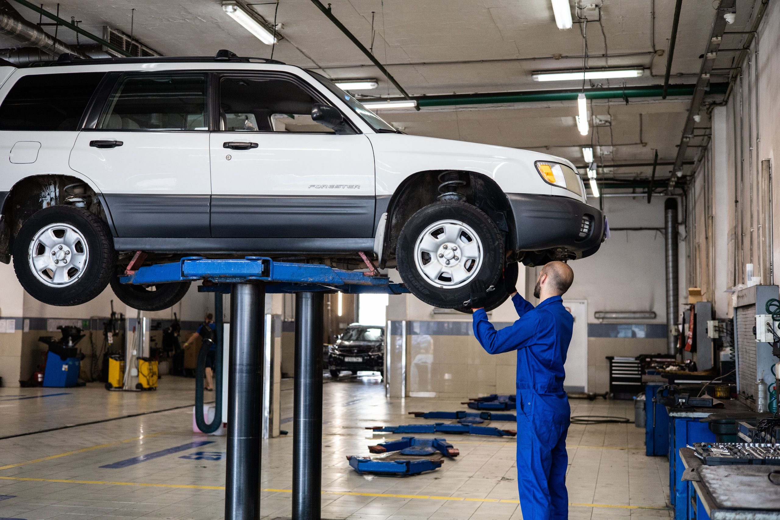 Mechanic inspecting the suspension of a lifted SUV in an auto repair shop.