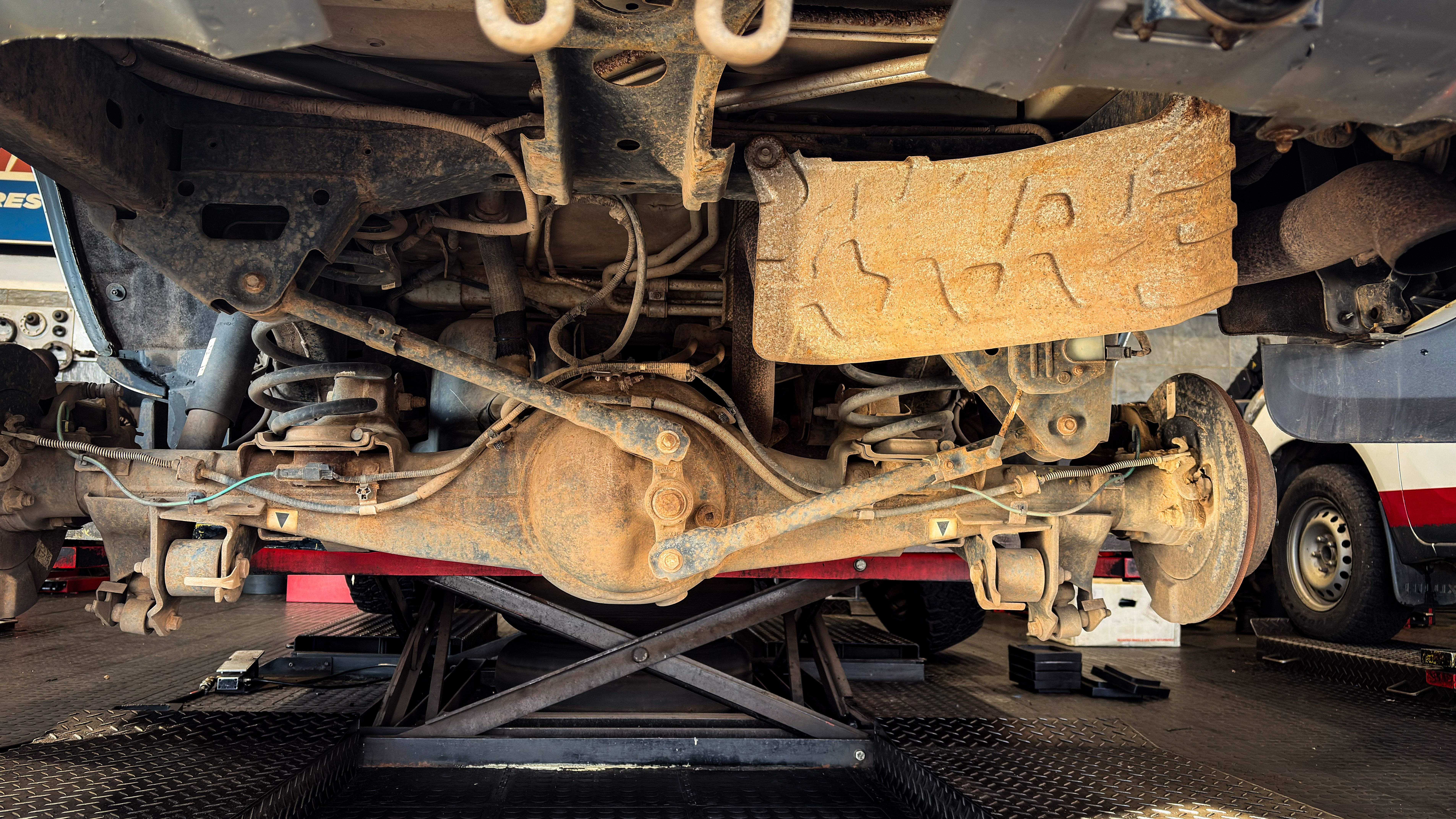 Close-up of a rusty vehicle suspension system being repaired in a garage.
