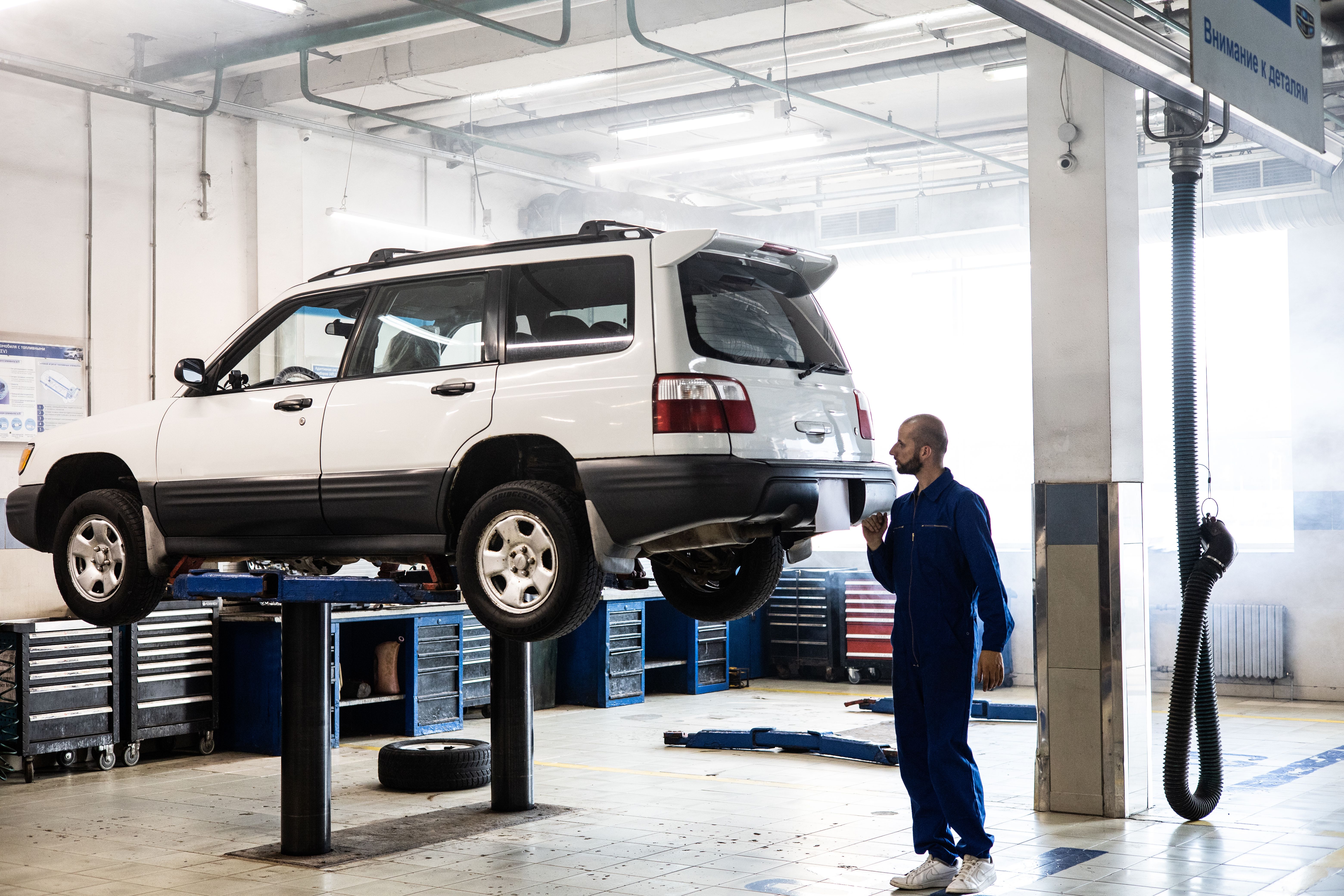 Mechanic examining the undercarriage of an SUV raised on a workshop lift.